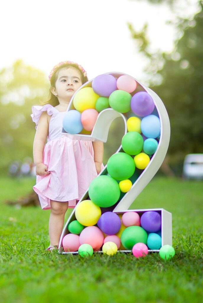 Young child celebrating a second birthday outdoors with colourful balloons