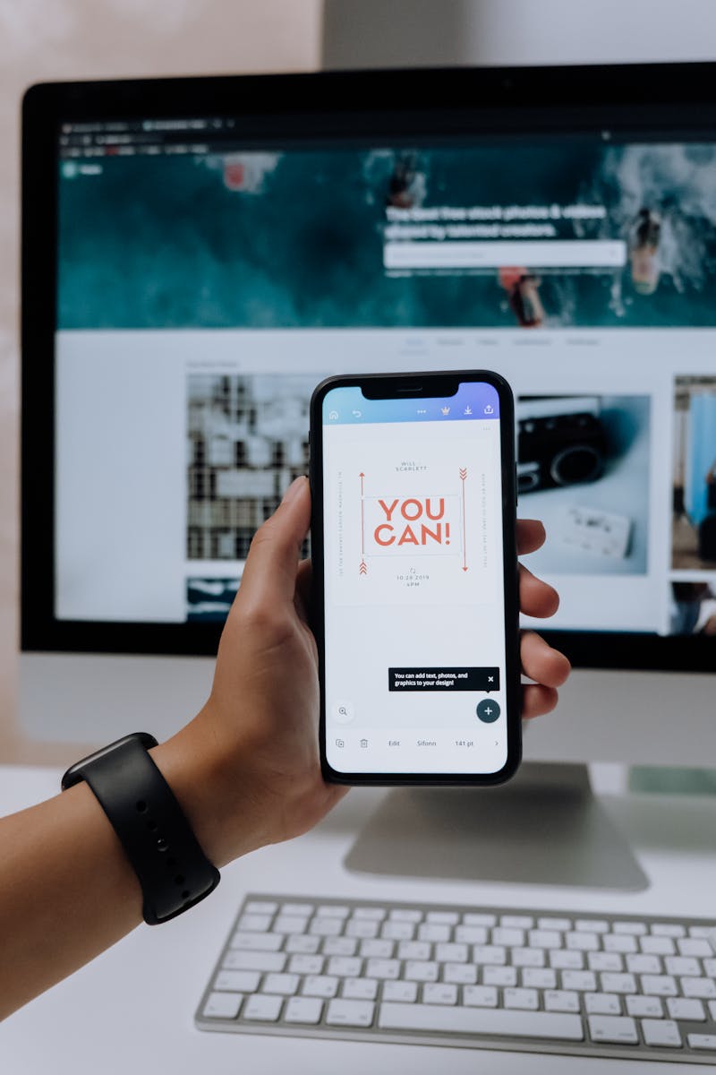 pexels-photo-5082580-5082580 Hand holding smartphone with 'You Can!' message in front of desktop screen.